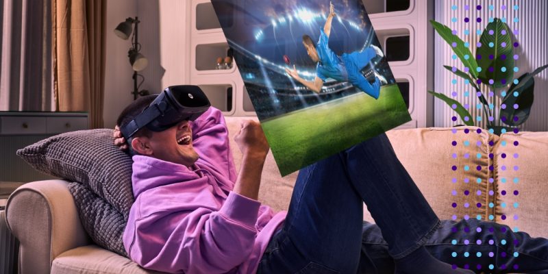 A man wearing JioDive VR Headsets enjoys a cricket match on his couch